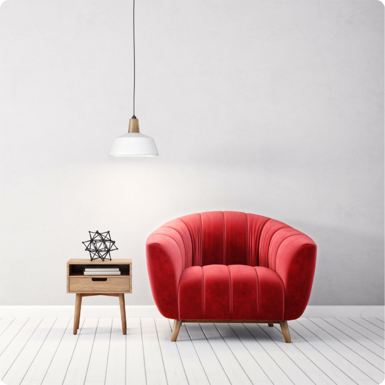 A red armchair sits next to a small wooden side table with decor, under a hanging white pendant light in a minimalist room.